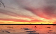 The sun sets as two people walk on the ice on White Bear Lake