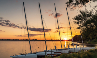 A row of catamarans float on White Bear Lake as the sun sets in the background.