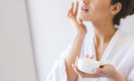 A woman applies a skin care product to her face.