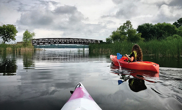 Two people paddle kayaks on White Bear Lake near the Manitou Island bridge.