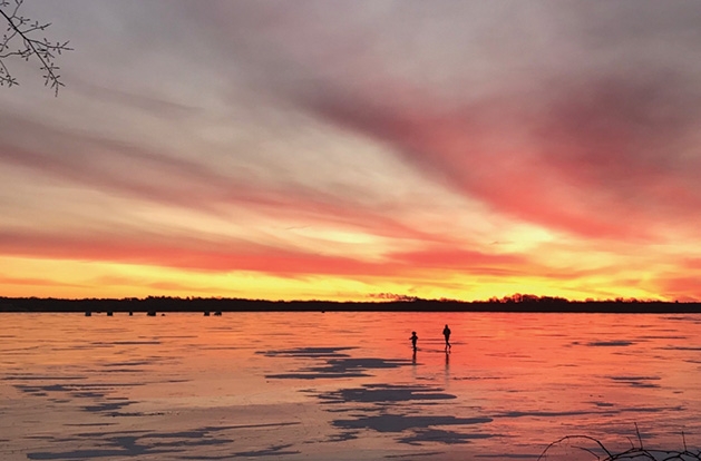 The sun sets as two people walk on the ice on White Bear Lake