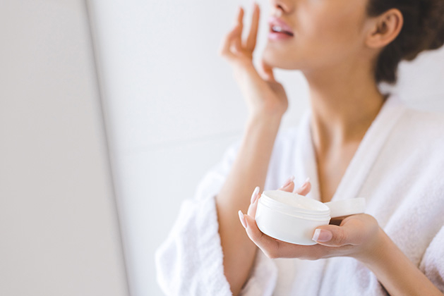 A woman applies a skin care product to her face.