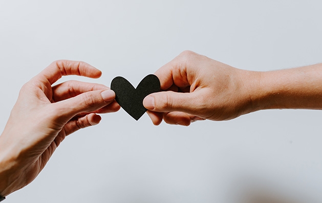 One hand hands another a black paper heart.