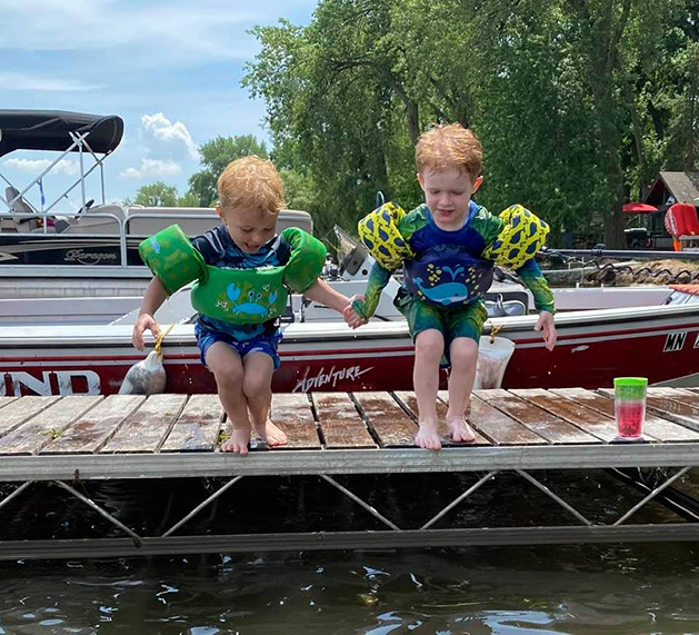Two young boys jump off a dock into a lake.